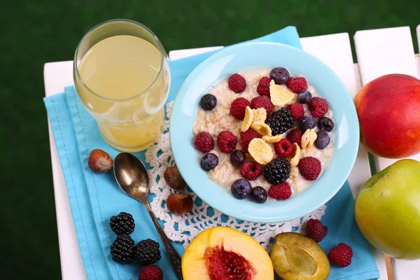 Oatmeal in plate with berries on napkin on table on grass background — Stock Photo, Image