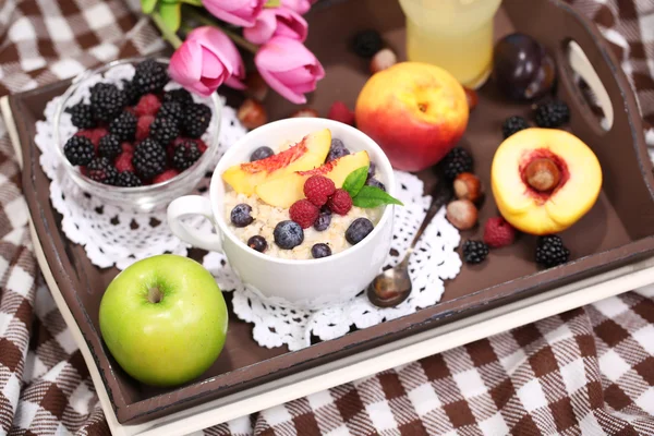 Oatmeal in plate with berries on napkins on wooden tray on bad — Stock Photo, Image