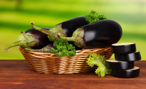 Fresh eggplants in wicker basket on table on wooden background — Stock Photo, Image