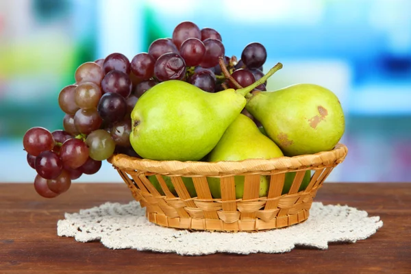 Pears and grape in wicker basket, on bright background — Stock Photo, Image