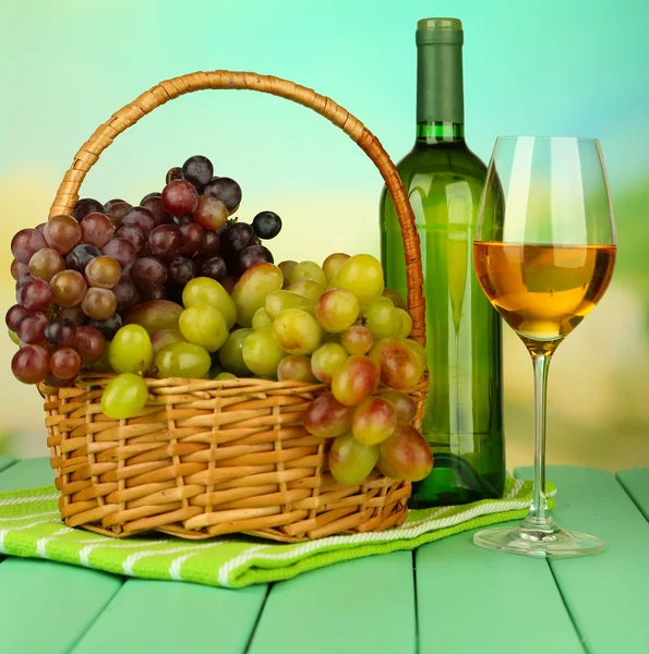 Ripe grapes in wicker basket, bottle and glass of wine, on bright background — Stock Photo, Image