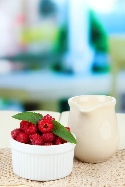 Fresh raspberry and cream in jug on wooden table, on bright background — Stock Photo, Image