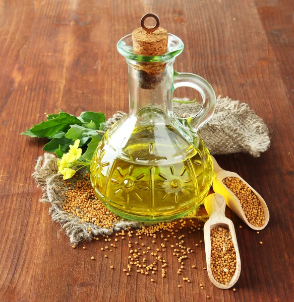 Jar of mustard oil and seeds with mustard flower on wooden background — Stock Photo, Image