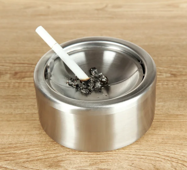 Metal ashtray and cigarette on wooden table — Stock Photo, Image