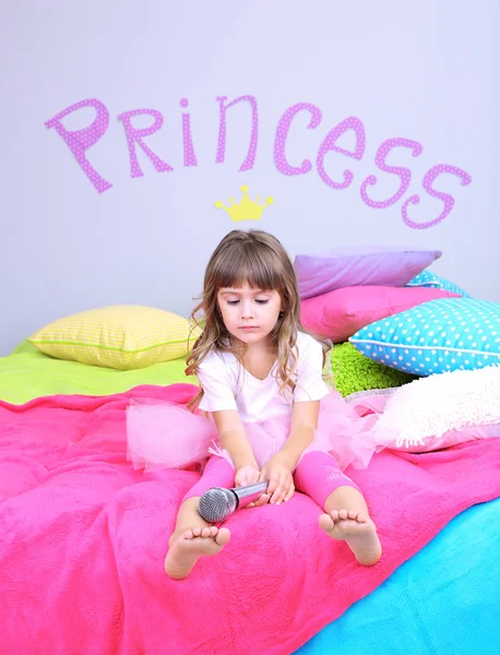 Little girl sings on bed in room on grey wall background — Stock Photo, Image