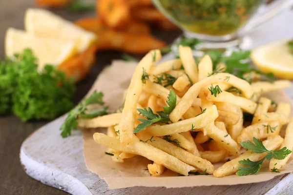 French fries on tracing paper on board on wooden table — Stock Photo, Image