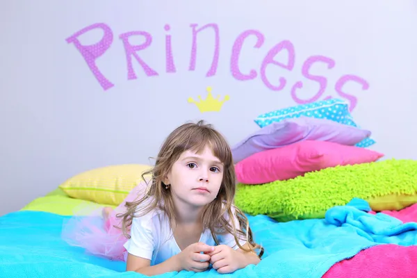 Little girl lying on bed in room on grey wall background — Stock Photo, Image