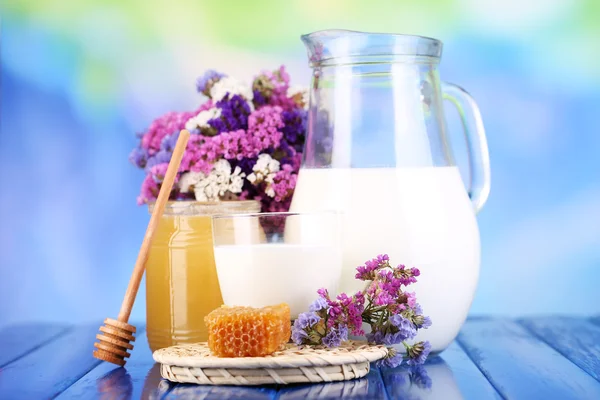 Honung och mjölk på träbord på blå bakgrund — Stockfoto