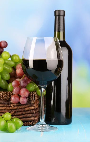 Ripe green and purple grapes in basket with wine on wooden table on natural background — Stock Photo, Image