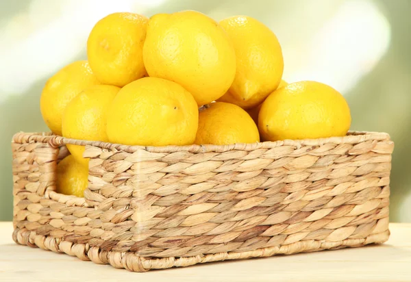 Reife Zitronen im Weidenkorb auf dem Tisch vor hellem Hintergrund — Stockfoto