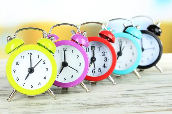 Relojes de alarma de colores en la mesa sobre fondo brillante — Foto de Stock