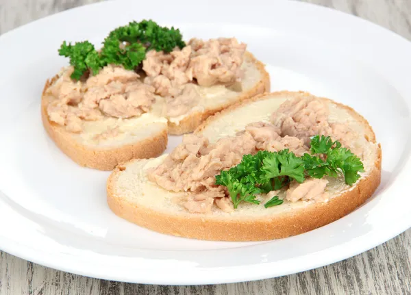 マグロやタラの肝臓のおいしいサンドイッチは白い皿にイワシします。木製の背景に — ストック写真