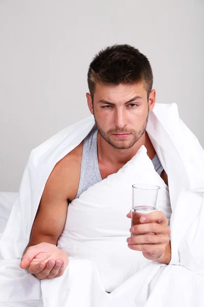 Hombre joven guapo con pastillas para dormir sobre fondo gris de la pared — Foto de Stock