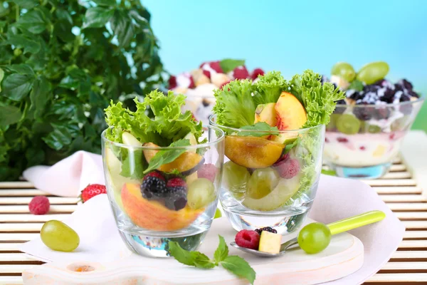Ensalada de frutas en vasos, sobre mesa de madera, sobre fondo brillante —  Fotos de Stock