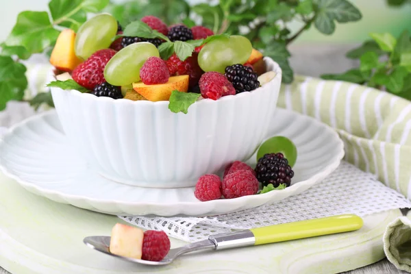 Salada de frutas na tigela, na mesa de madeira, no fundo brilhante — Fotografia de Stock