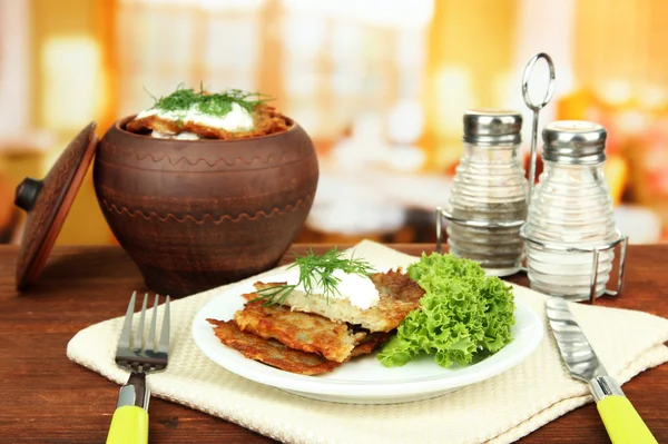 Aardappelpannenkoekjes in pot, op houten tafel, op lichte achtergrond — Stockfoto