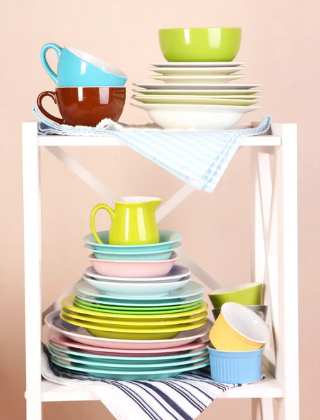 Beautiful white shelves with tableware and decor, on color wall background, close-up — Stock Photo, Image