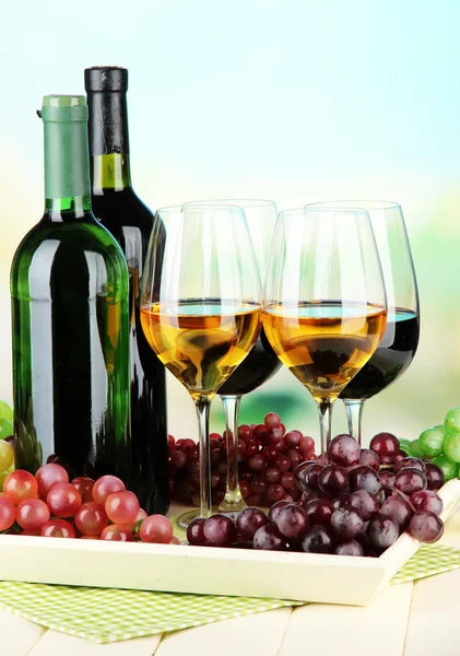 Wine bottles and glasses of wine on tray, on bright background — Stock Photo, Image