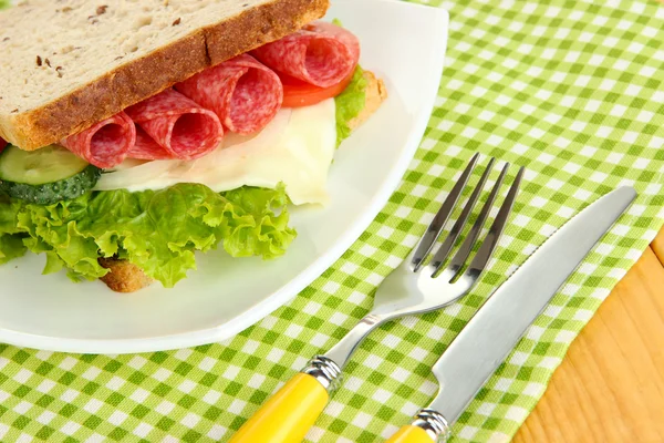 Sanduíche saboroso com salsicha de salame e legumes na placa branca, no fundo de madeira — Fotografia de Stock