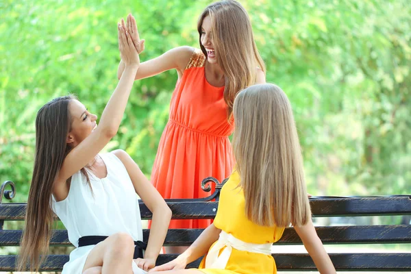 Tre vakre, unge kvinner sitter på benken i sommerparken. – stockfoto