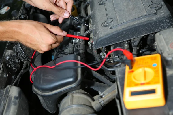Mecánico automático utiliza voltímetro multímetro para comprobar el nivel de voltaje en la batería del coche —  Fotos de Stock