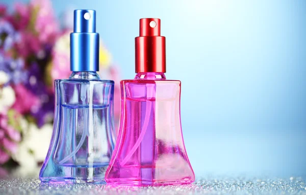 Perfumy kobiety w pięknych butelkach i kwiaty na niebieskim tle — Zdjęcie stockowe