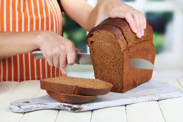 Cutting bread on wooden board on wooden table on window background — Stock Photo, Image