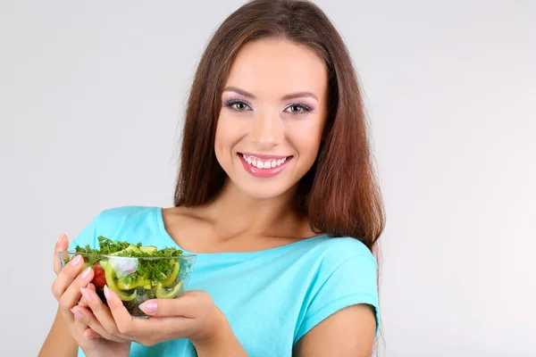 Menina bonita com salada fresca no fundo cinza — Fotografia de Stock