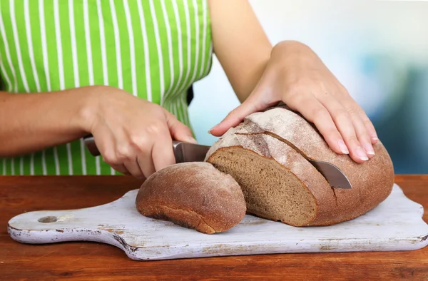 Cutting bread on wooden board on wooden table on natural background — Stock Photo, Image