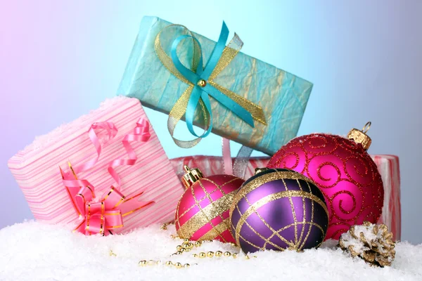 Beautiful Christmas balls and gifts on snow on bright background — Stockfoto