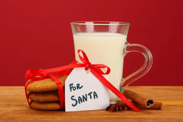 Kekse für den Weihnachtsmann: Konzeptbild von Ingwerplätzchen, Milch und Weihnachtsdekoration auf rotem Hintergrund — Stockfoto