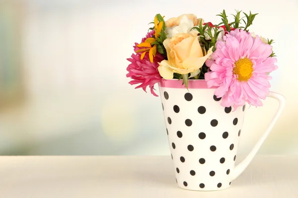 Gyönyörű csokor, világos virágok, színes bögre, fából készült asztal, a világos háttér — Stock Fotó