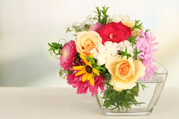 Beautiful bouquet of bright flowers in glass vase, on wooden table, on bright background — Stock Photo, Image