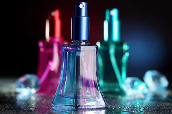 Perfume de las mujeres en hermosas botellas sobre fondo oscuro con luz de color — Foto de Stock