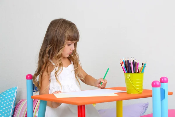 Menina desenha sentado à mesa no quarto no fundo da parede cinza — Fotografia de Stock