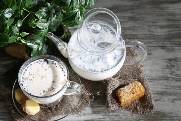 Teapot and cup of tea with milk and spices on sackcloth of wooden table — Stock Photo, Image