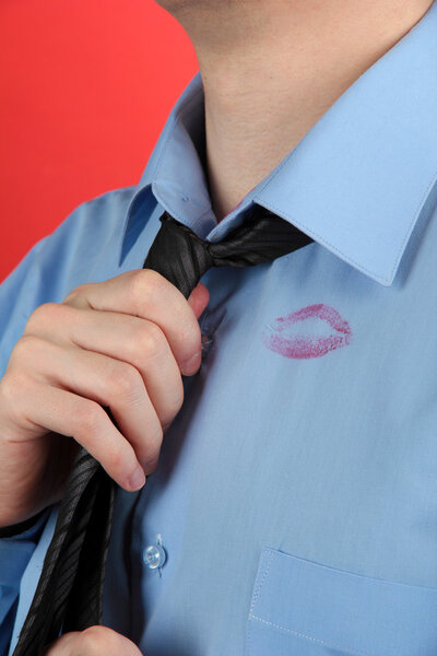 Lipstick kiss on shirt collar of man, on red background