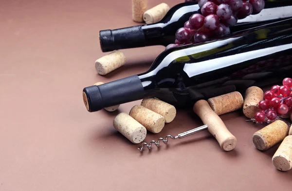 Bottles of wine, grapes and corks on brown background — Stock Photo, Image