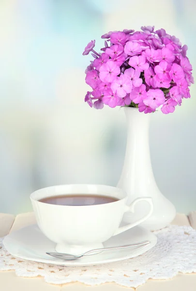 Schöner Phlox-Strauß mit einer Tasse Tee auf dem Tisch auf hellem Hintergrund — Stockfoto