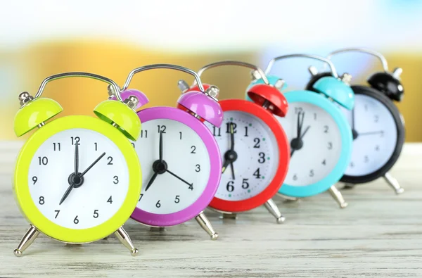 Relojes de alarma de colores en la mesa sobre fondo brillante — Foto de Stock