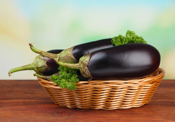 Fresh eggplants in wicker basket on table on wooden background — Stock Photo, Image
