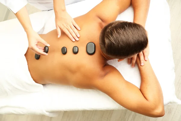 Ung man med sten massage i spasalong — Stockfoto