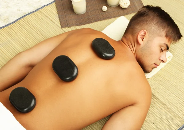 Młody człowiek relaksujący z gorącymi kamieniami na powrót przed masażu — Zdjęcie stockowe