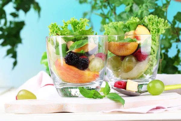 Salada de fruto em copos, em mesa de madeira, em fundo brilhante — Fotografia de Stock