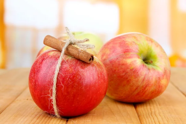 Спелые яблоки с коричными палочками на деревянном столе, на ярком фоне — стоковое фото