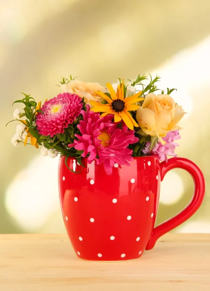 Bellissimo bouquet di fiori luminosi in tazza di colore, su tavolo di legno, su sfondo luminoso — Foto Stock