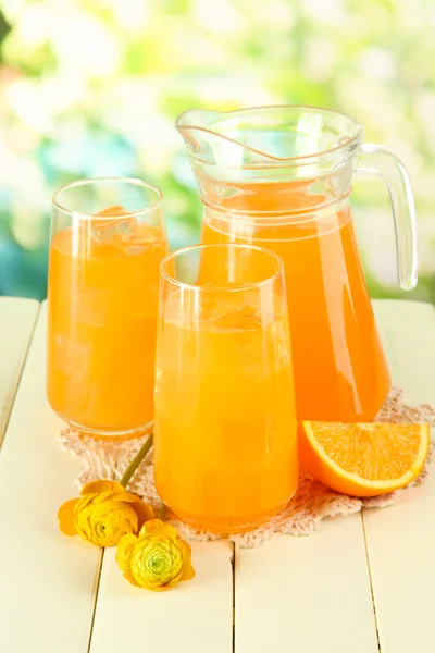 メガネと緑色の背景で、木製のテーブルの上のオレンジ ジュースの投手 — ストック写真