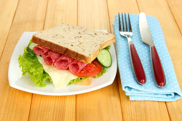 Sanduíche saboroso com salsicha de salame e legumes na placa branca, no fundo de madeira — Fotografia de Stock