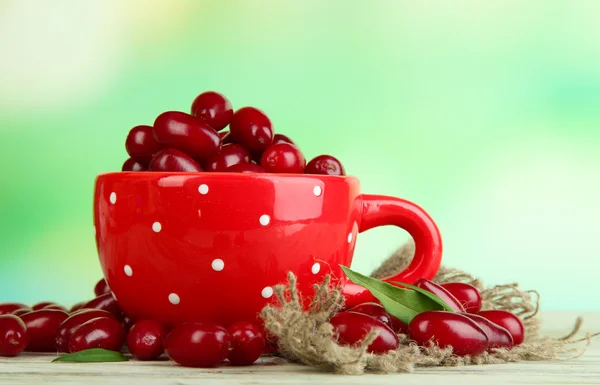Cornel świeże jagody w czerwony kubek na drewnianym stole — Zdjęcie stockowe