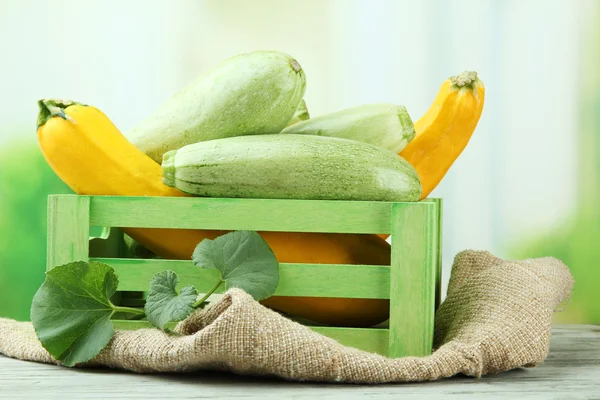 Sliced and whole raw zucchini in wooden crate, outdoors — Stock Photo, Image